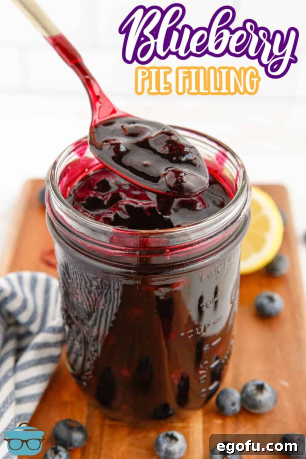 Pinterest image of Blueberry Pie Filling in mason jar with spoon holding some up with blueberries and lemon in background.