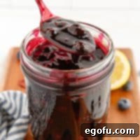 Square image of Blueberry Pie Filling in mason jar with spoon holding some of the filling up.