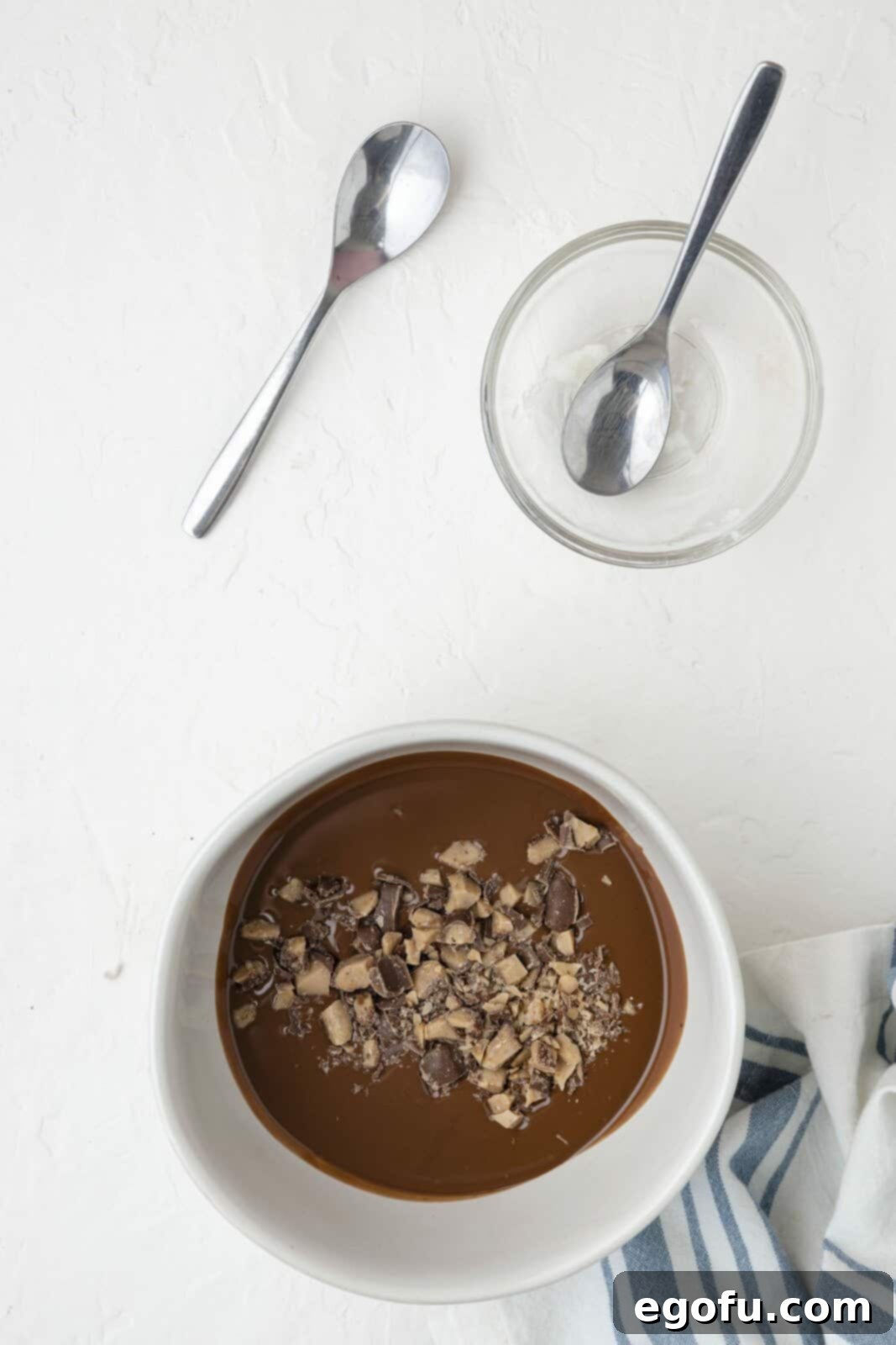 Generous pieces of crushed Heath bar being carefully stirred into the warm, melted chocolate and coconut oil mixture, creating a textural and flavorful blend.