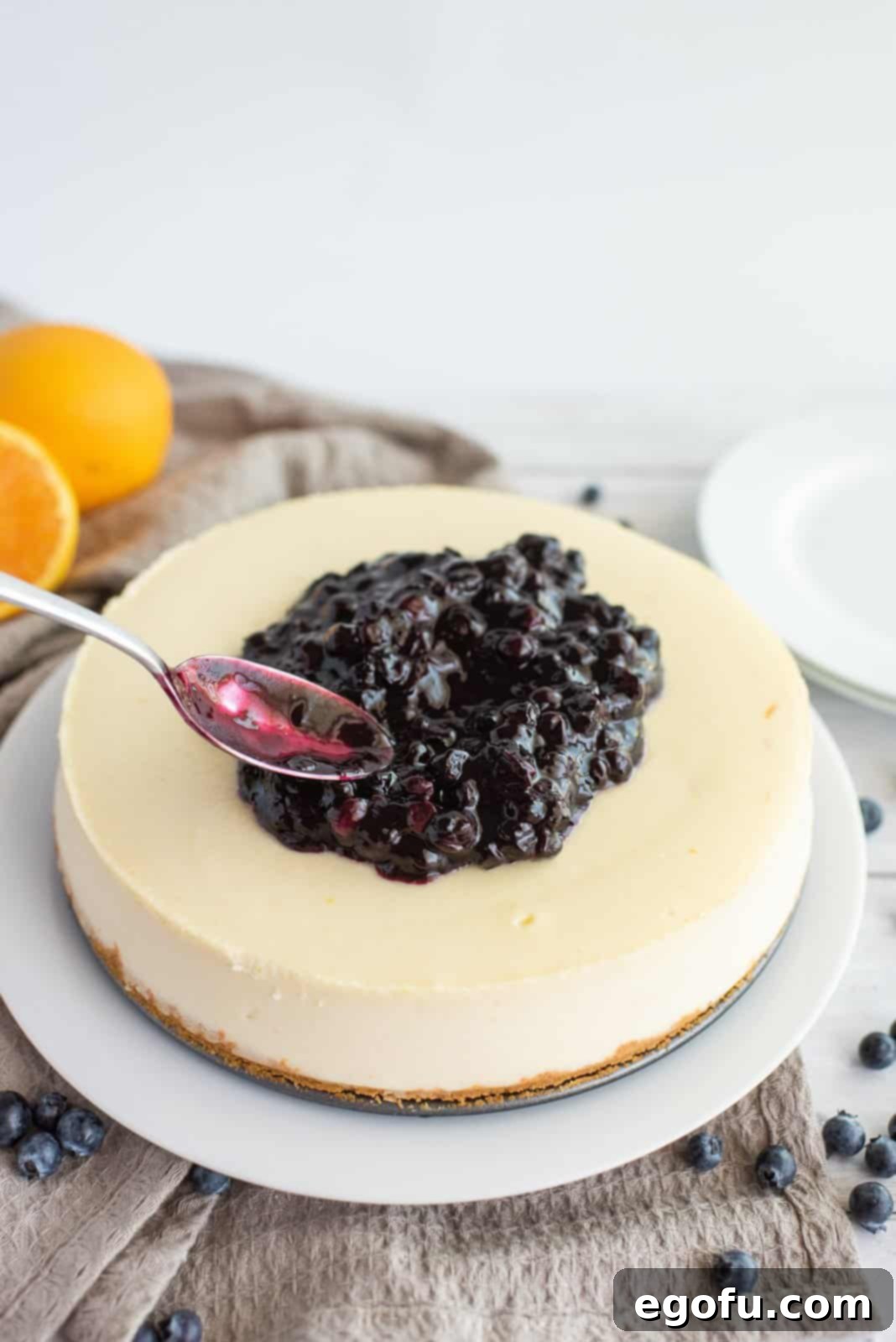 Blueberry sauce being spread over finished cheesecake.