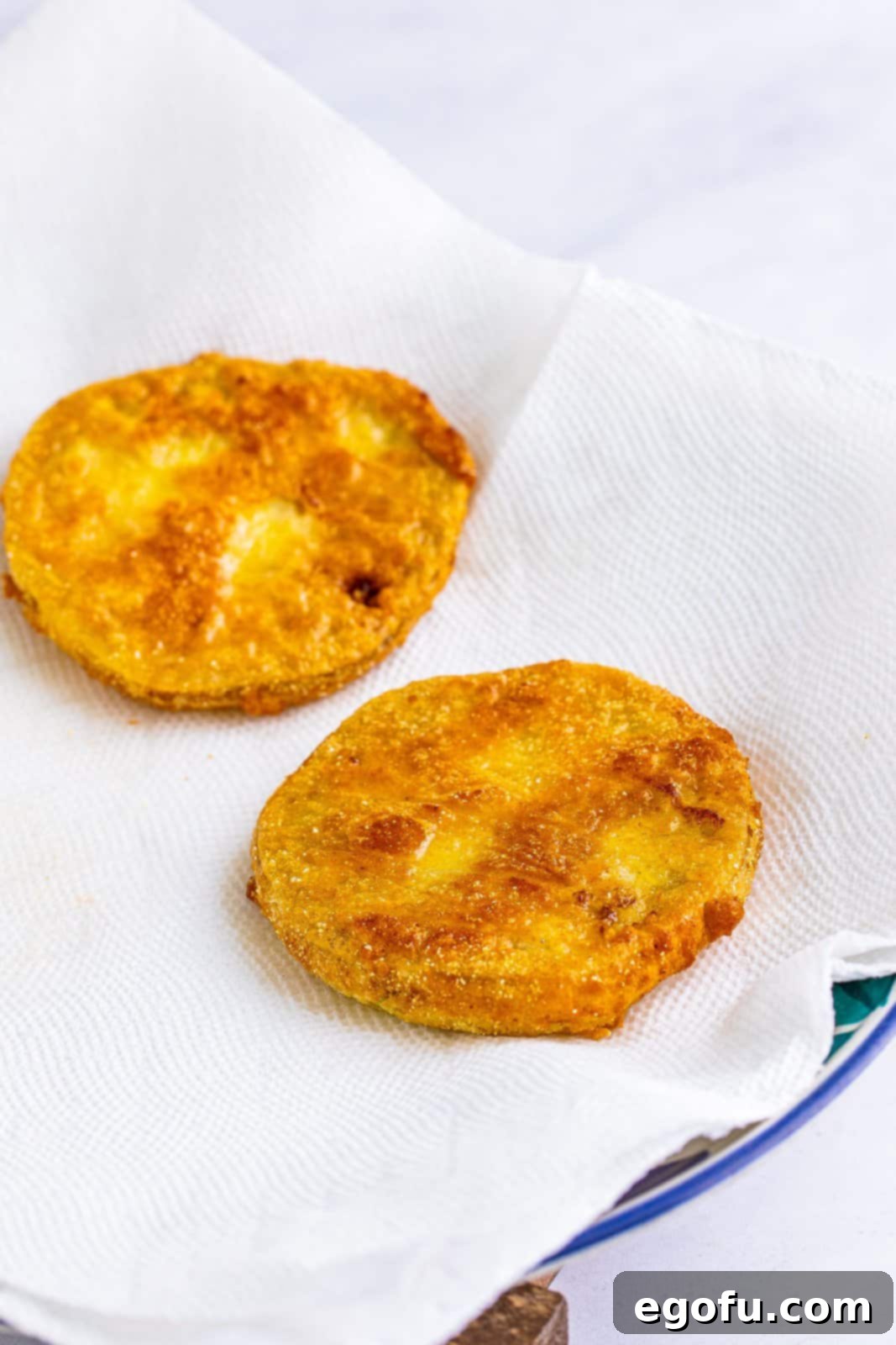 Freshly fried green tomatoes rest on a paper towel-lined plate, allowing excess oil to drain away, a crucial step for achieving perfectly crisp results.