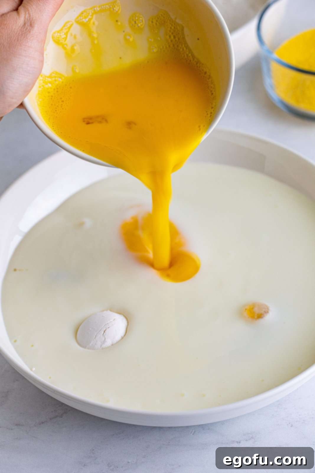 Beaten eggs are carefully added to a bowl containing buttermilk and a vibrant mix of spices, preparing the wet coating for the fried green tomatoes.