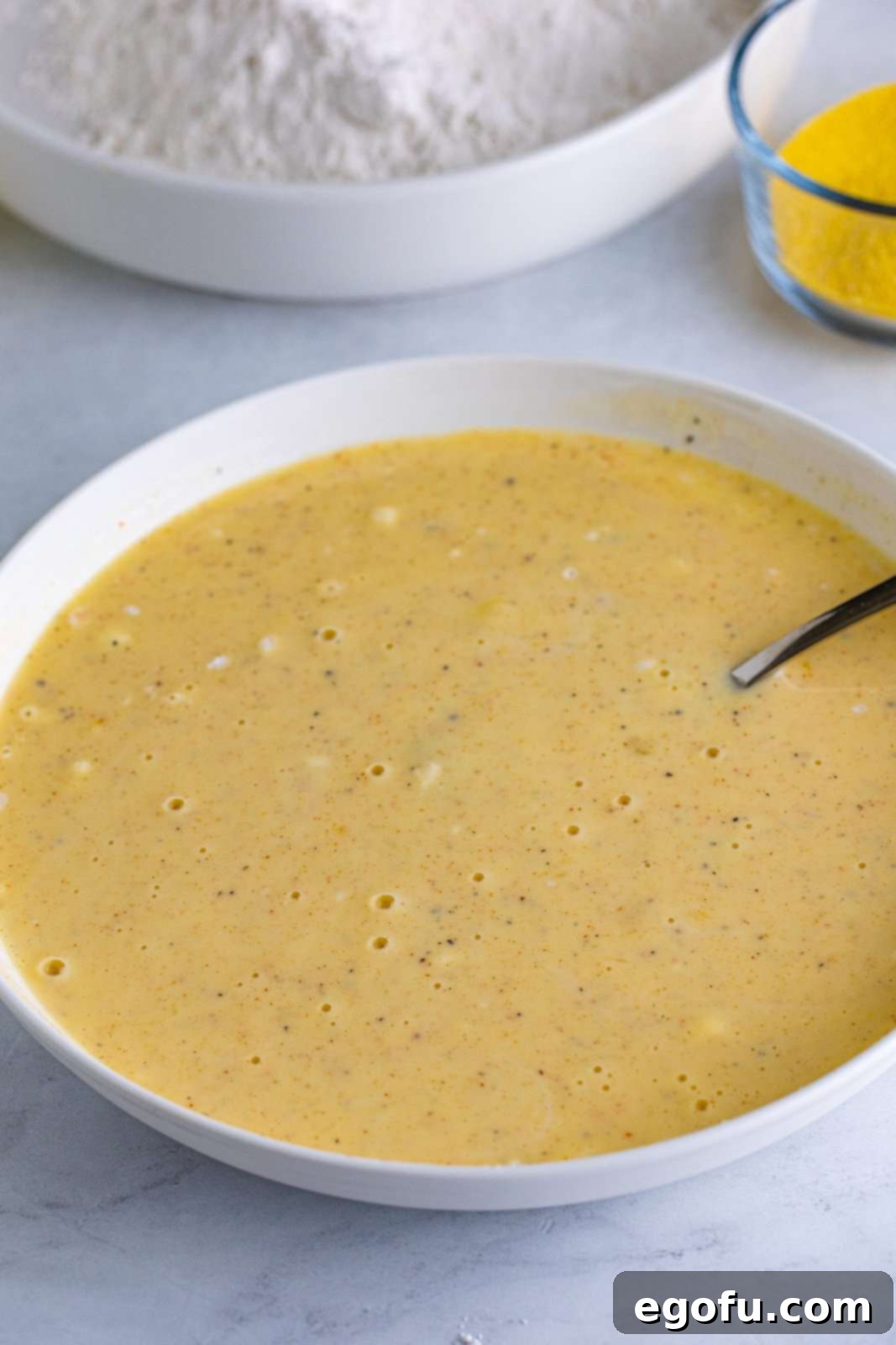 The buttermilk mixture, enriched with eggs and spices, is expertly stirred until smooth and perfectly combined, ready for the next step in preparing fried green tomatoes.