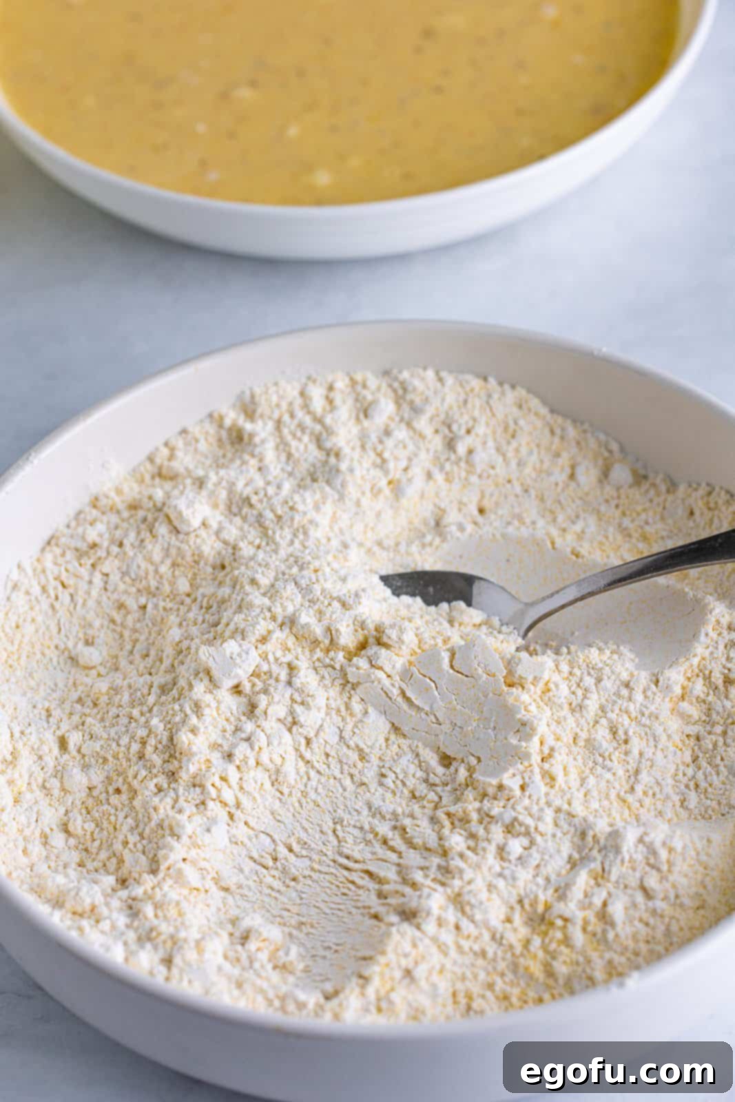 Self-rising flour and yellow cornmeal are carefully stirred together in a bowl, creating the essential dry coating mixture for crispy fried green tomatoes.