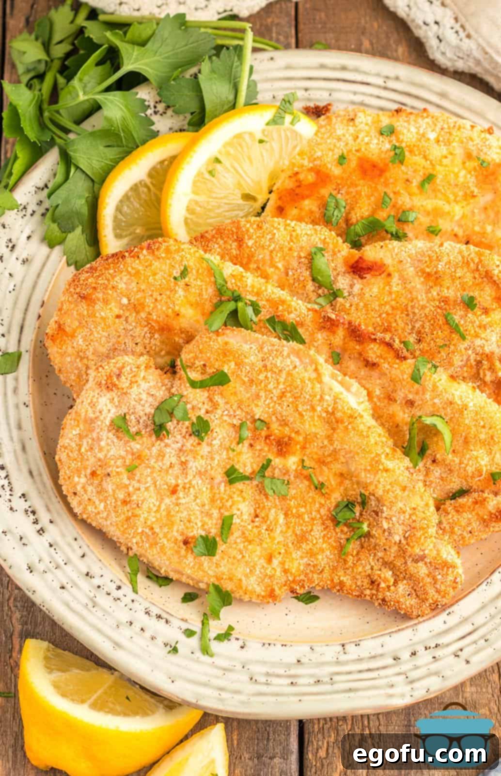 Overhead of layered Air Fryer Chicken Cutlets on plate with lemon wedges and parsley.