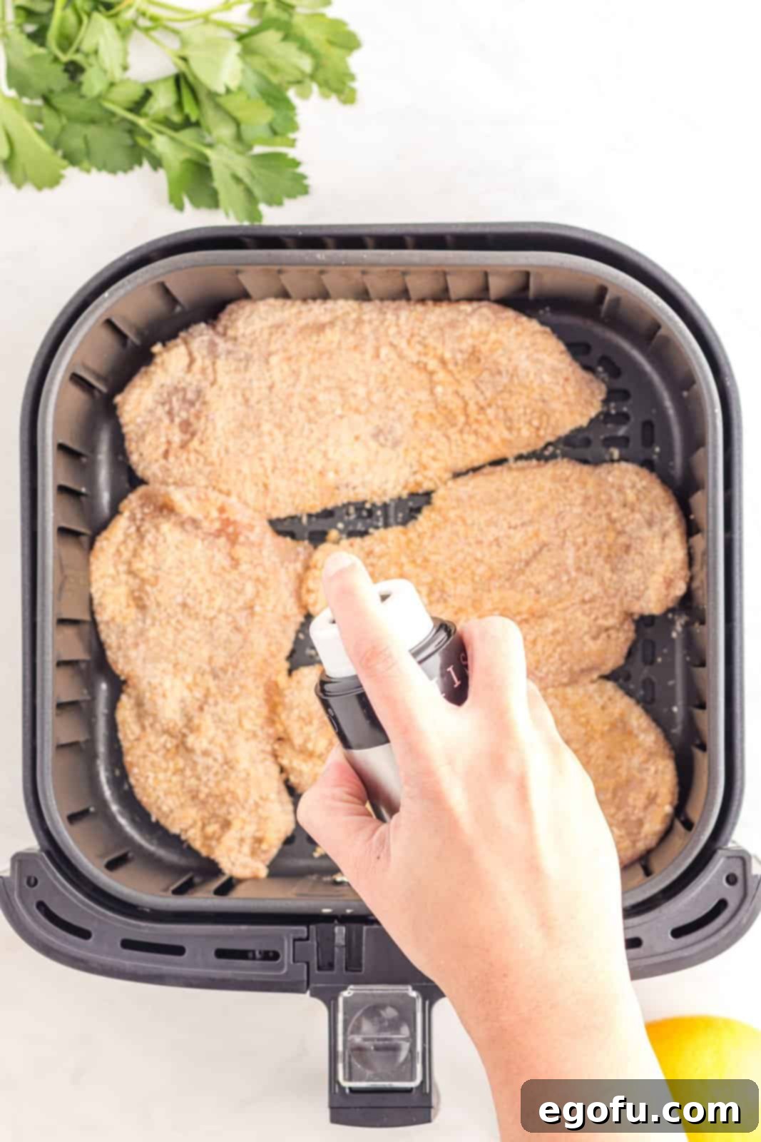 Cutlets being sprayed with olive oil spray.