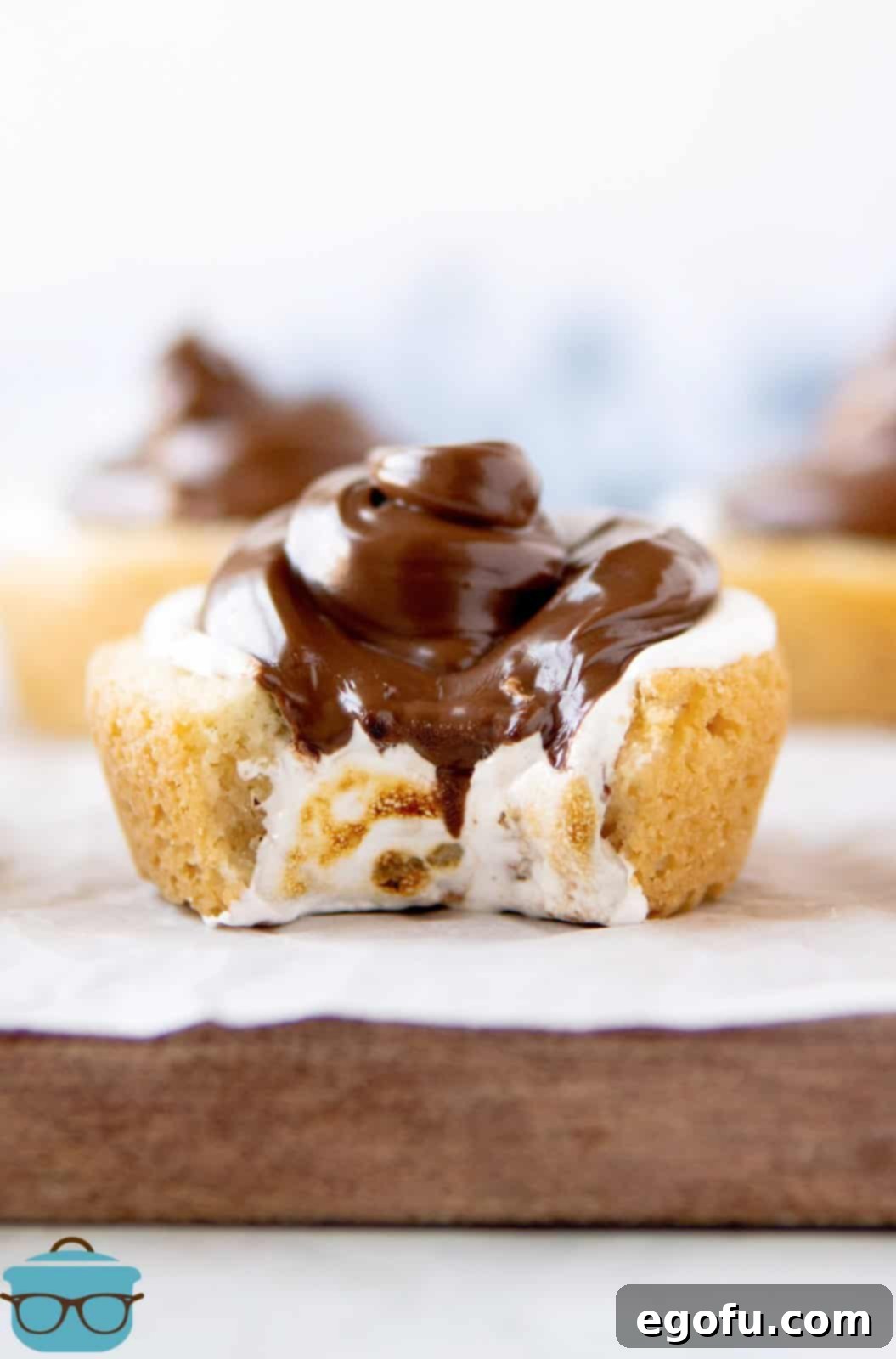 S'mores Cookie Cups on wooden board with parchment paper with bite taken out of it.