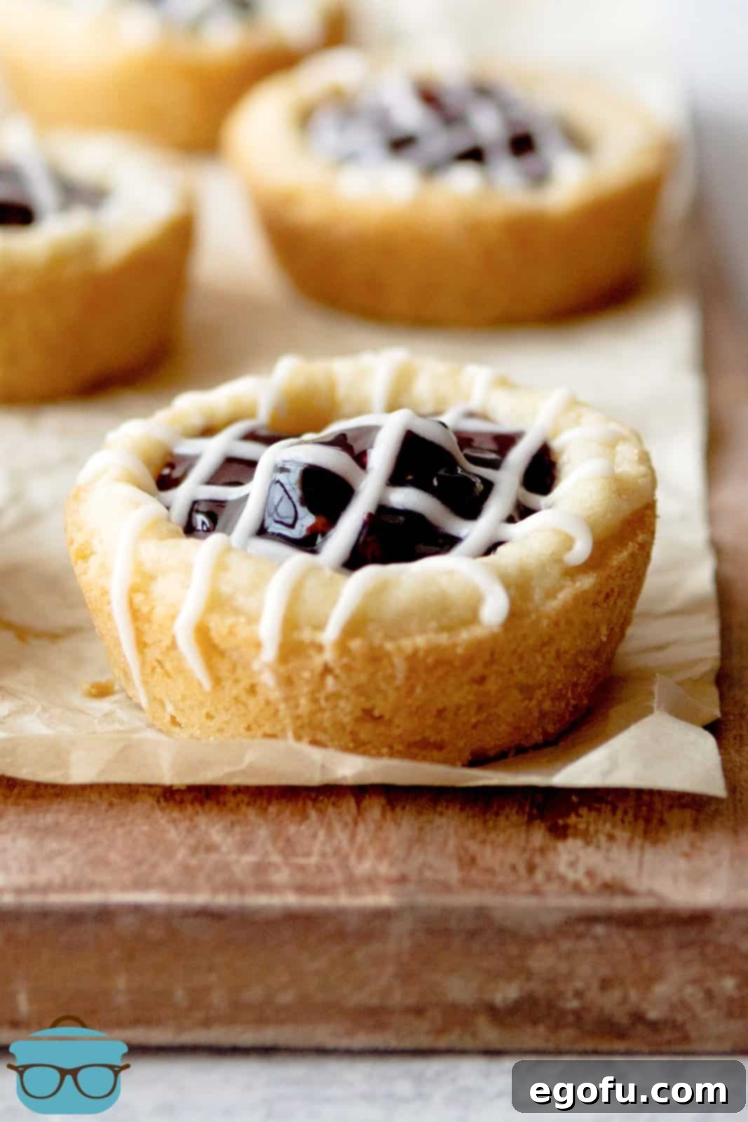 Berry Burst Cookie Cups 2 Freshly baked Berry Cookie Cups resting on parchment paper, beautifully drizzled with a sweet glaze, highlighting their vibrant berry filling.