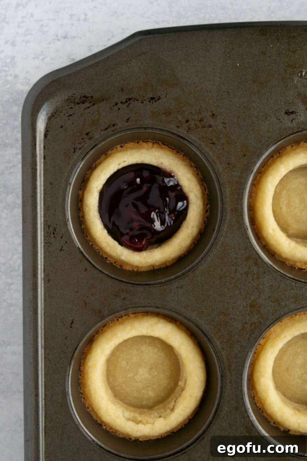 Berry Burst Cookie Cups 8 Sweet mixed berry pie filling being carefully spooned into the warm, golden cookie cups nestled in a muffin pan.