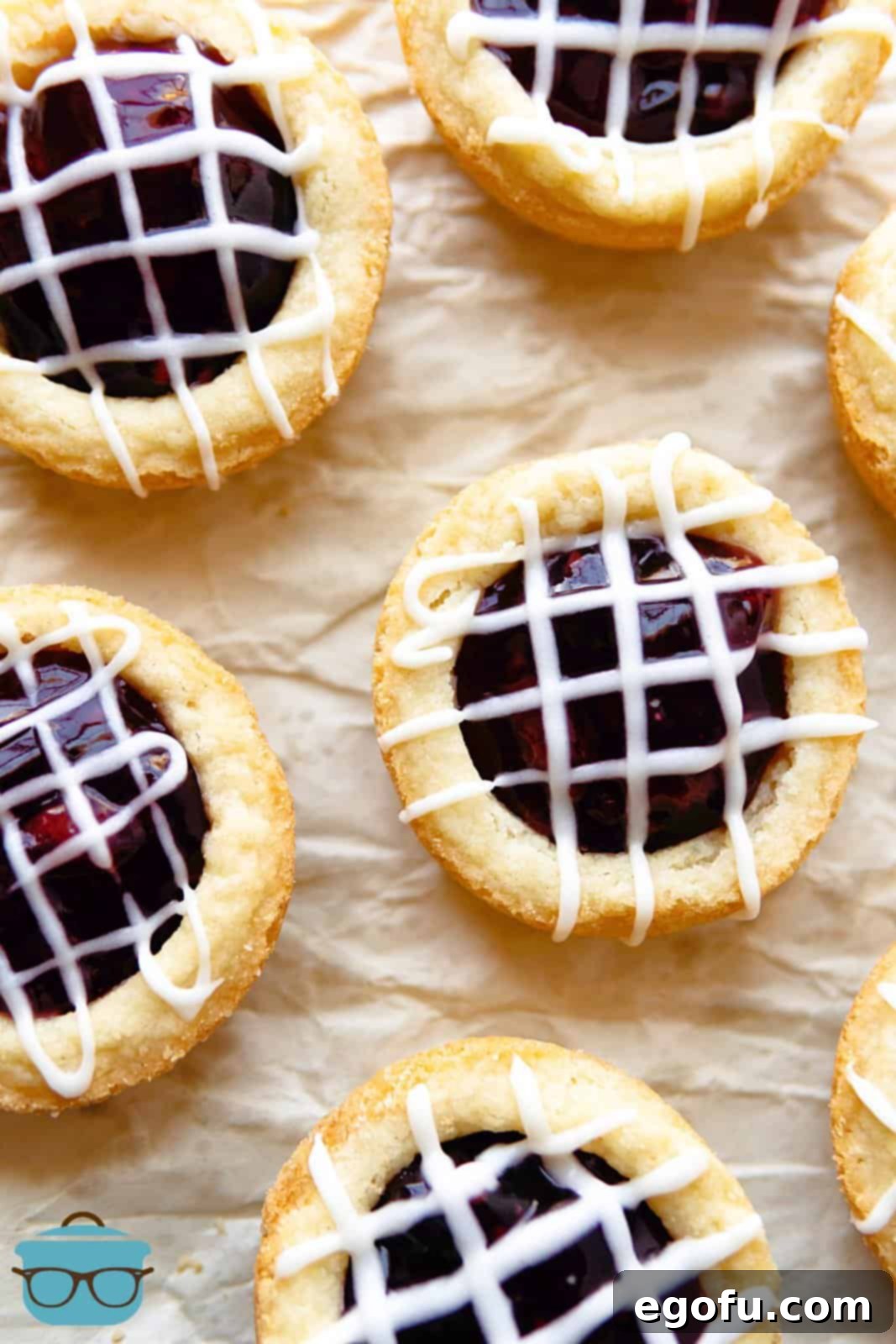 Berry Burst Cookie Cups 9 An inviting overhead view of Berry Cookie Cups arranged on parchment paper, each exquisitely drizzled with a smooth, white glaze.