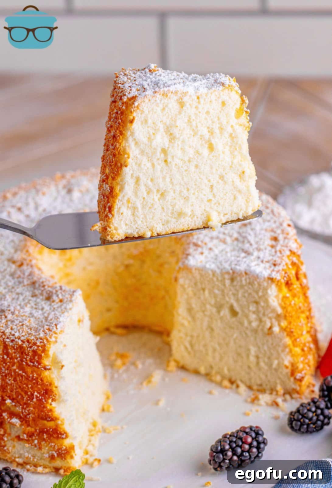A whole homemade Angel Food Cake with a single slice removed, revealing its airy interior.