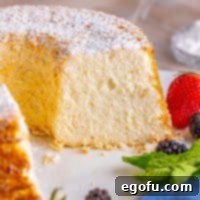 A homemade angel food cake on a white platter with a slice removed.