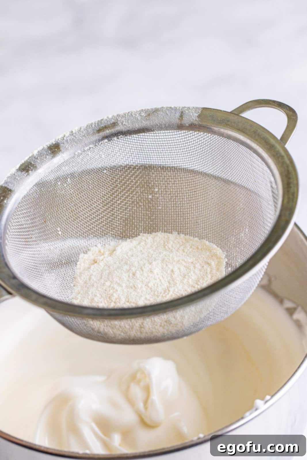 Flour and sugar mixture being carefully sifted and folded into egg whites.