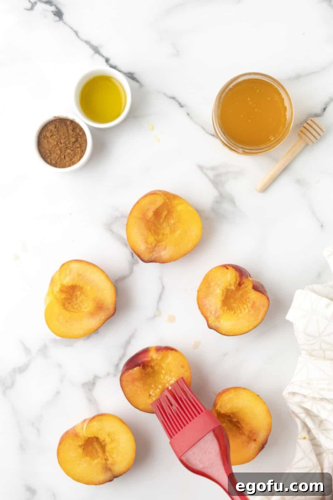 Peaches cut in half with pit removed being brushed with oil, demonstrating even coating.