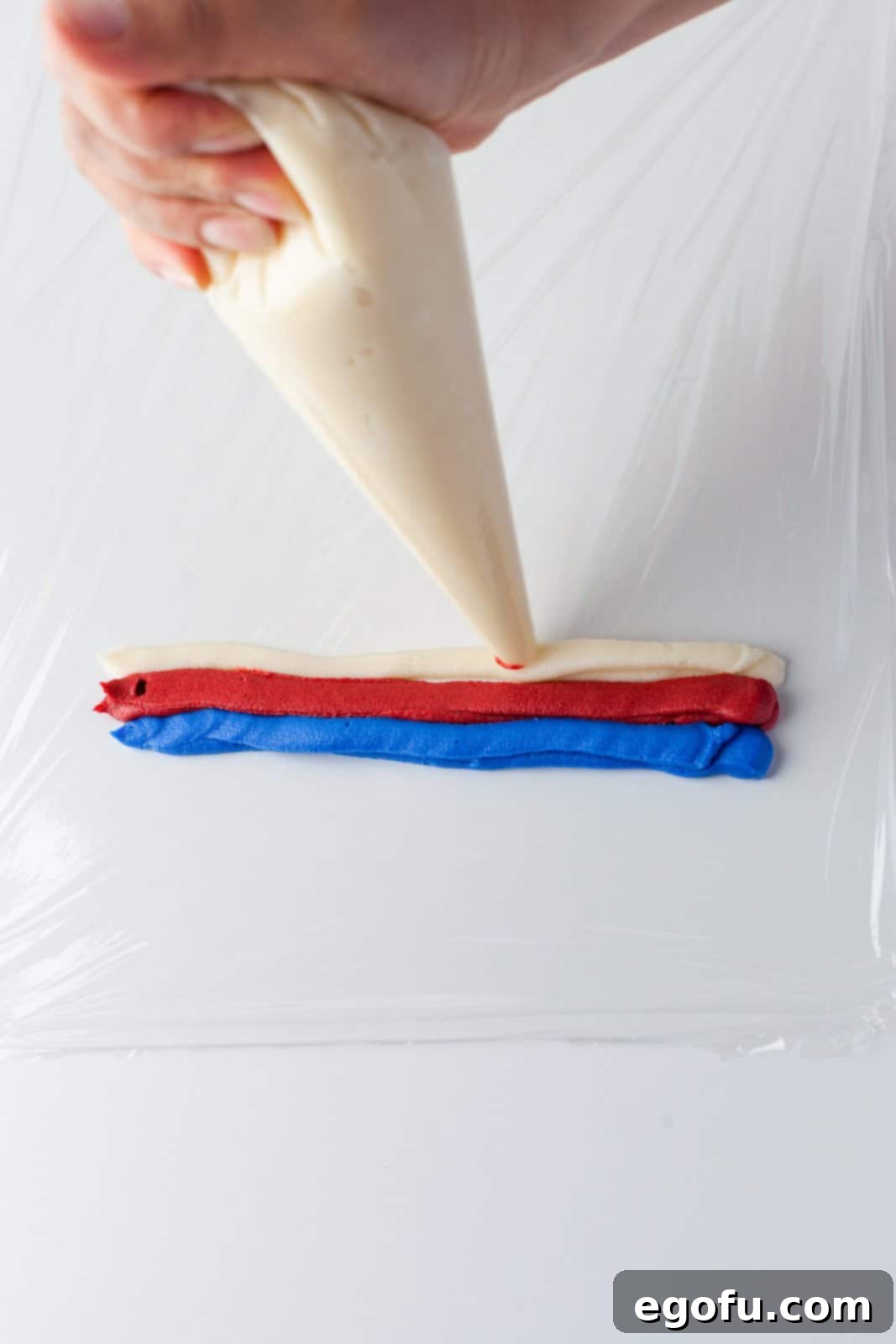Colors of frosting being piped onto plastic wrap.