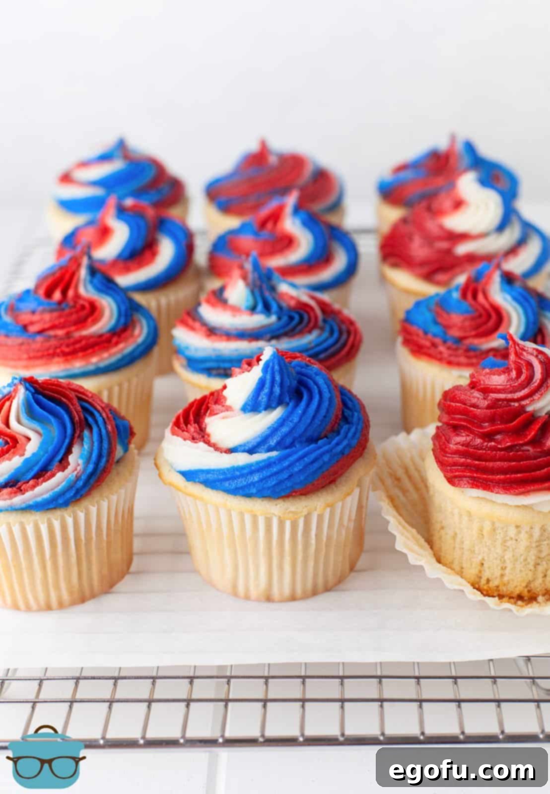 Finished 4th of July Cupcakes on parchment paper on wire rack lined up in rows.