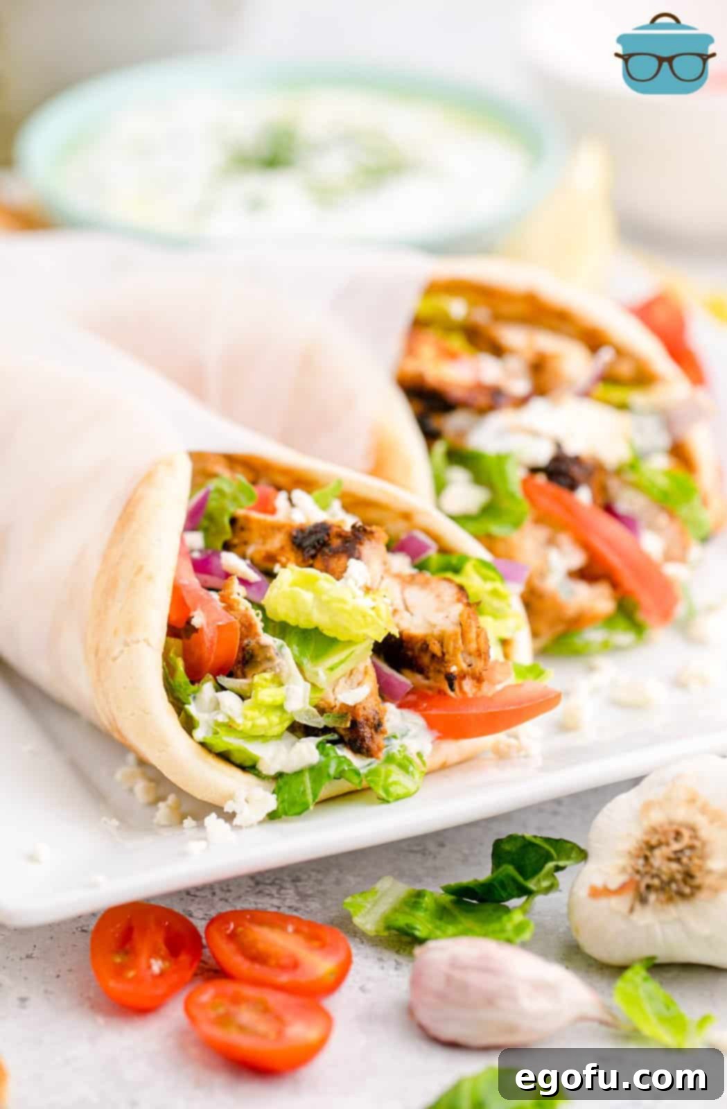 Two Greek Chicken Gyros on a white platter, wrapped in parchment paper, ready to serve.