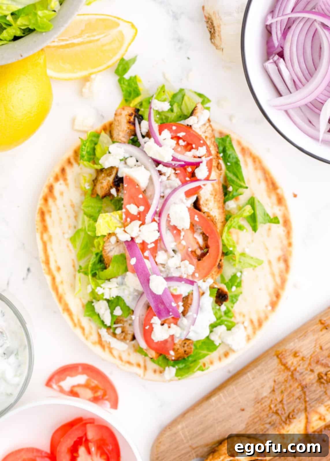 Pita bread filled with chicken, lettuce, onion, tomatoes, and tzatziki sauce, ready to be folded.