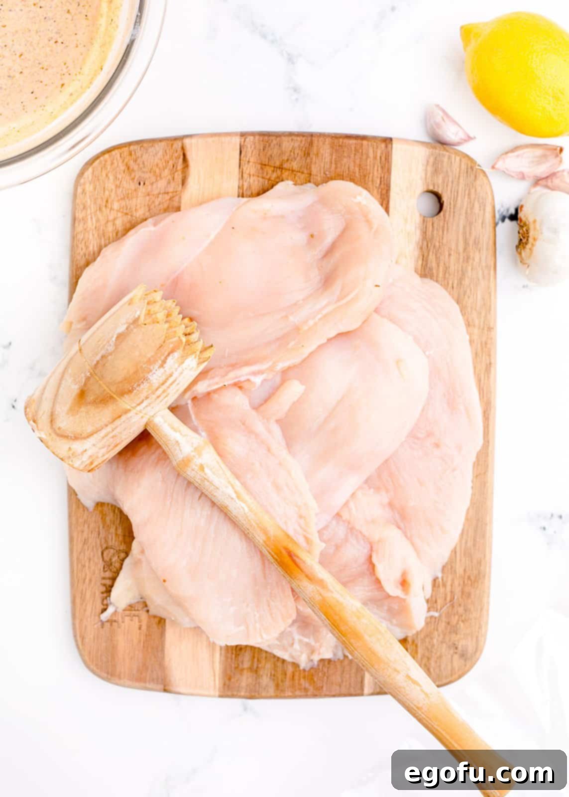 Chicken being pounded out on cutting board to an even thickness.