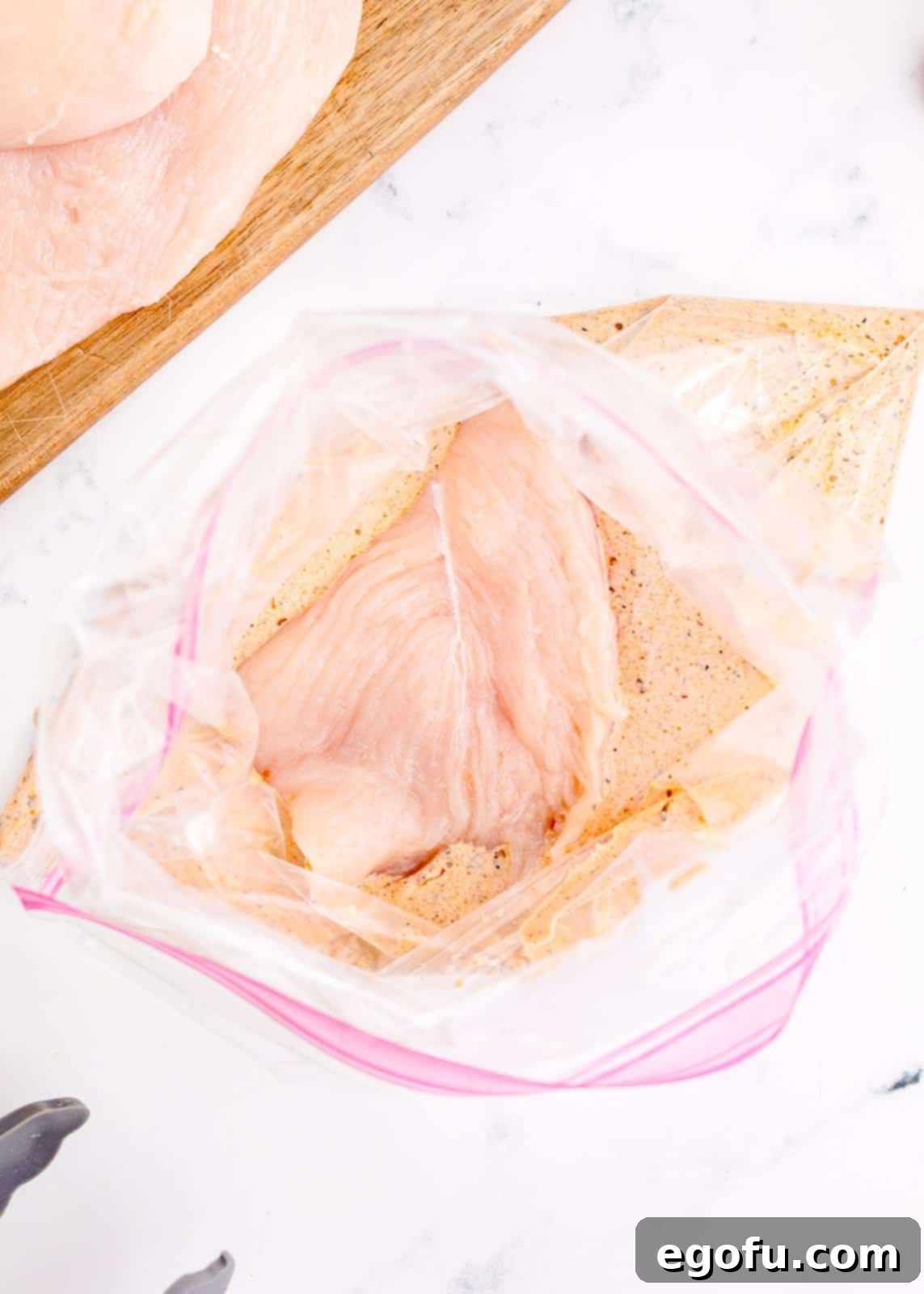 Chicken placed into a plastic bag with marinade, being massaged to ensure even coating.