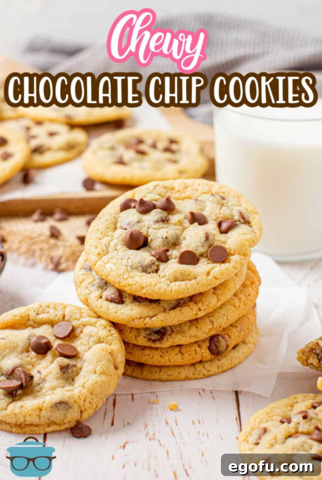 A high-angle shot of perfectly stacked chewy chocolate chip cookies on parchment paper, with a glass of milk in the background.