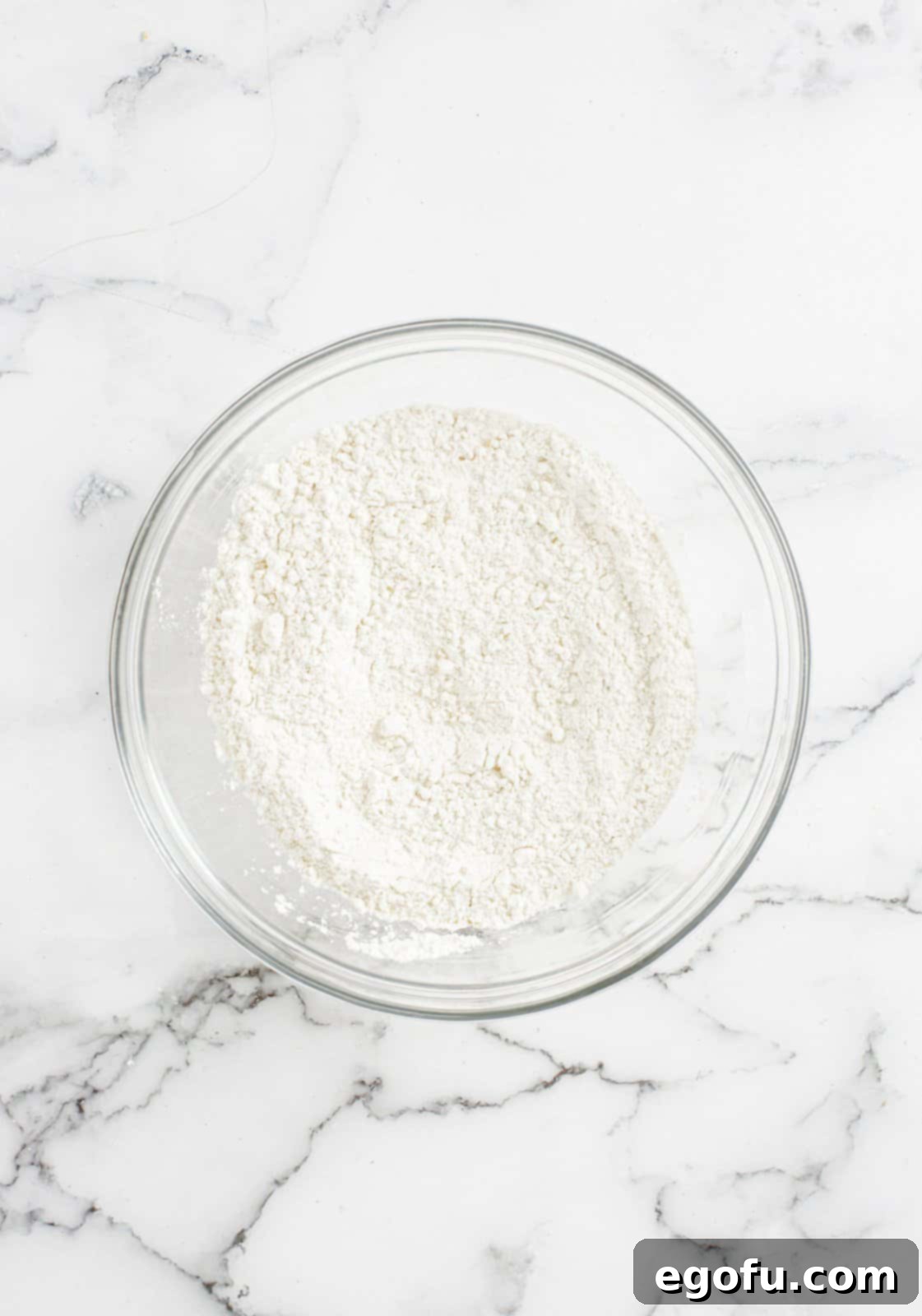 A bowl containing flour, baking soda, and salt, perfectly whisked together.