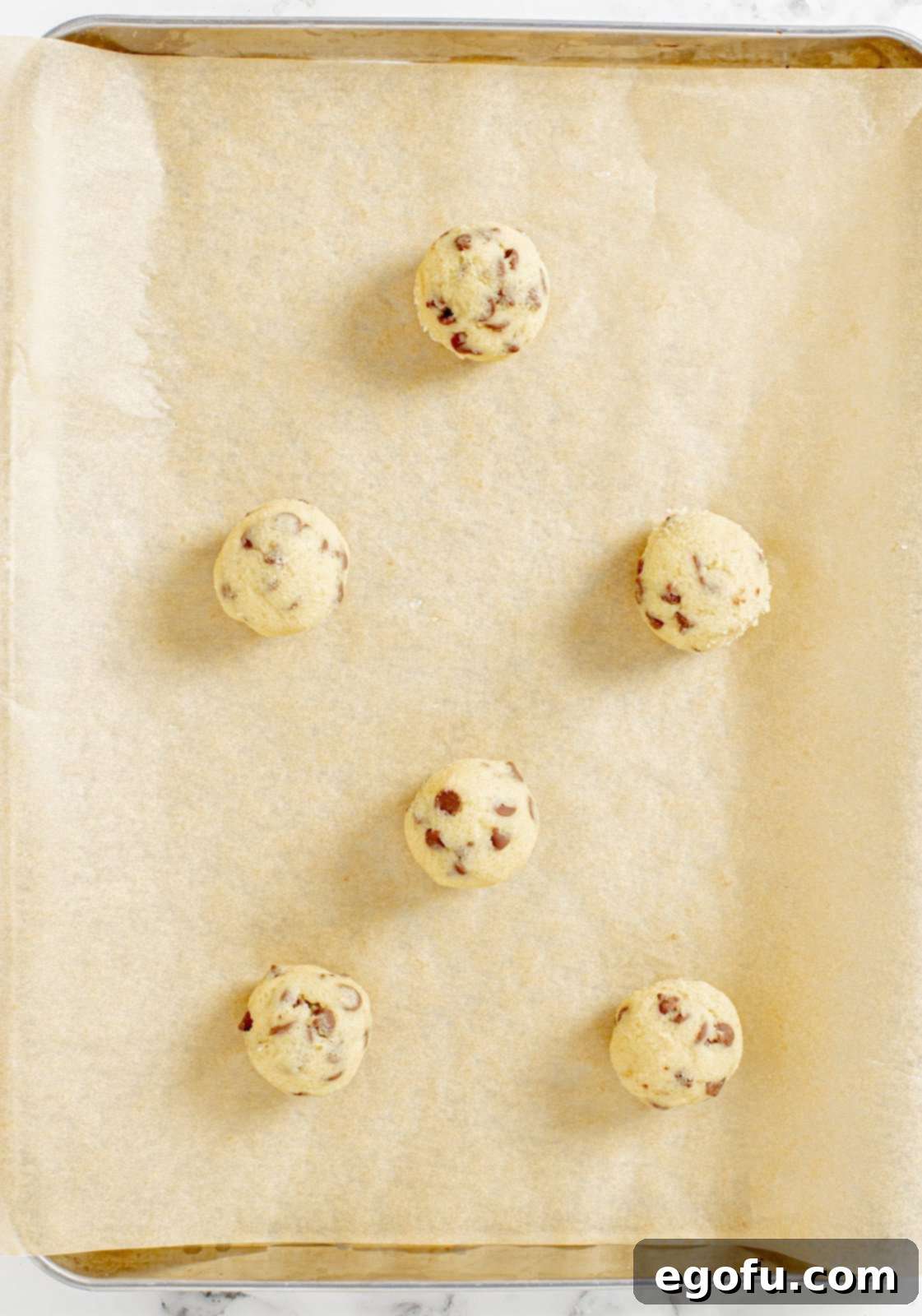 Portioned and rolled cookie dough balls neatly arranged on a parchment-lined baking sheet.