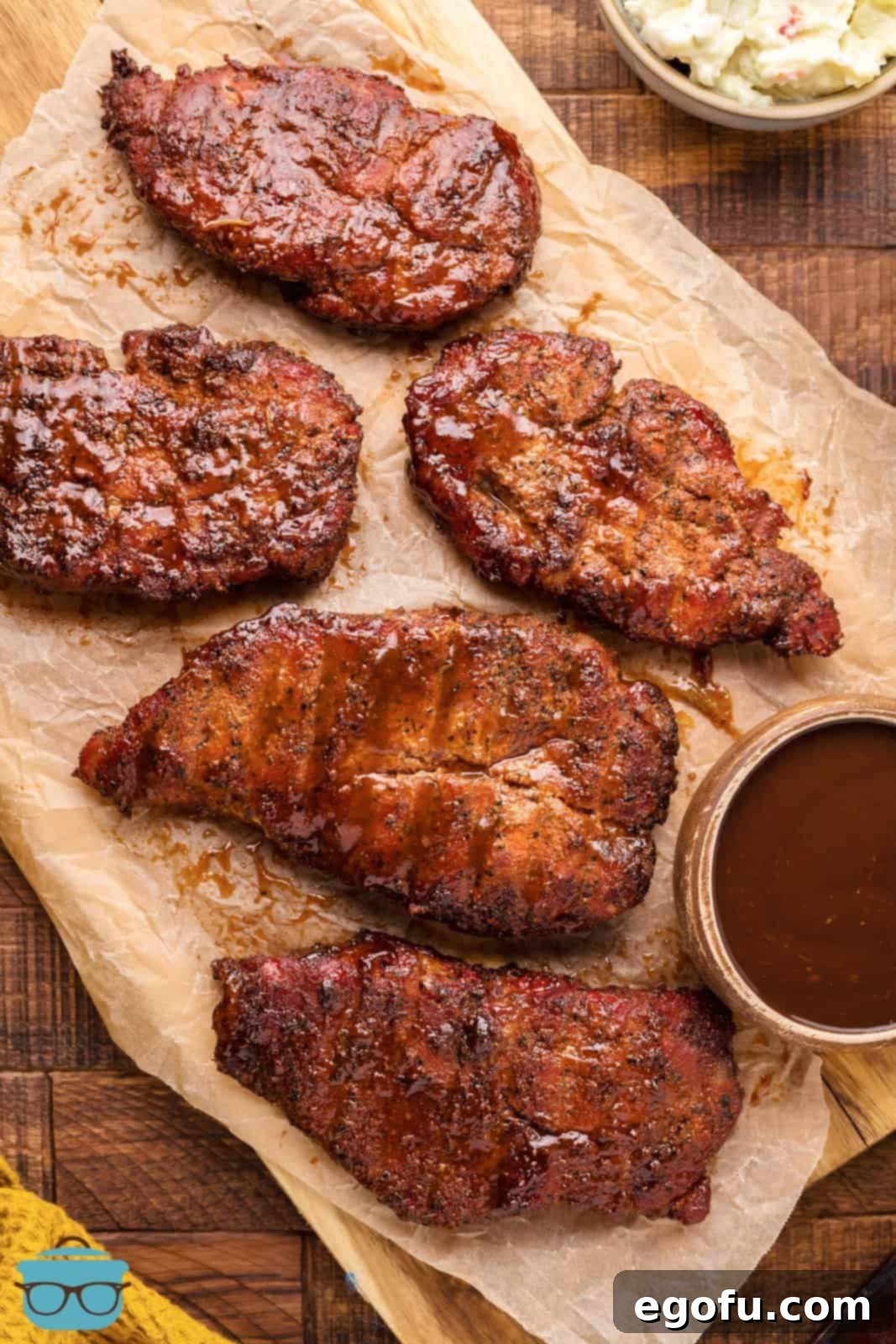 Smoked Pork Steaks overhead on butcher paper with BBQ sauce on side.