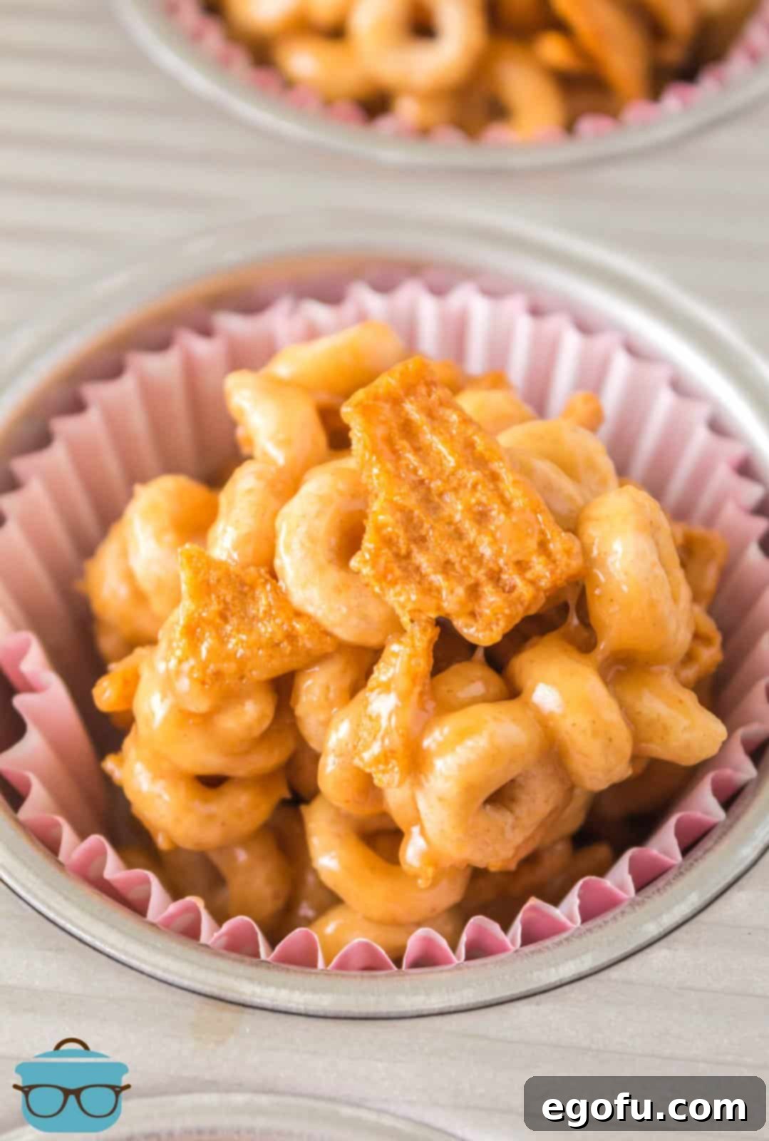 Close-up of a single finished Peanut Butter Cheerio Ball in a muffin tin liner, showing its irresistible texture.