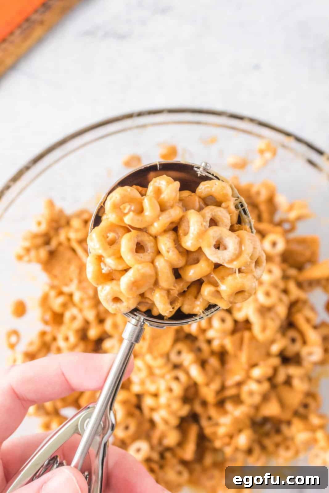 A large cookie scoop holding a portion of the mixed cereal and peanut butter mixture, ready to be formed into a ball.