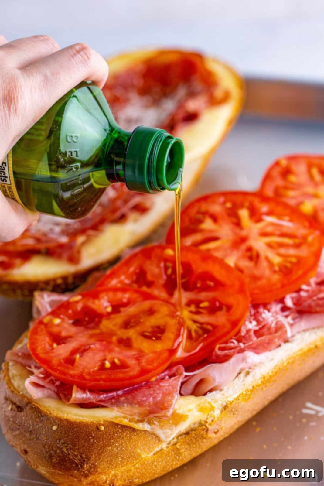 drizzling olive oil over sliced tomatoes on a sub roll.