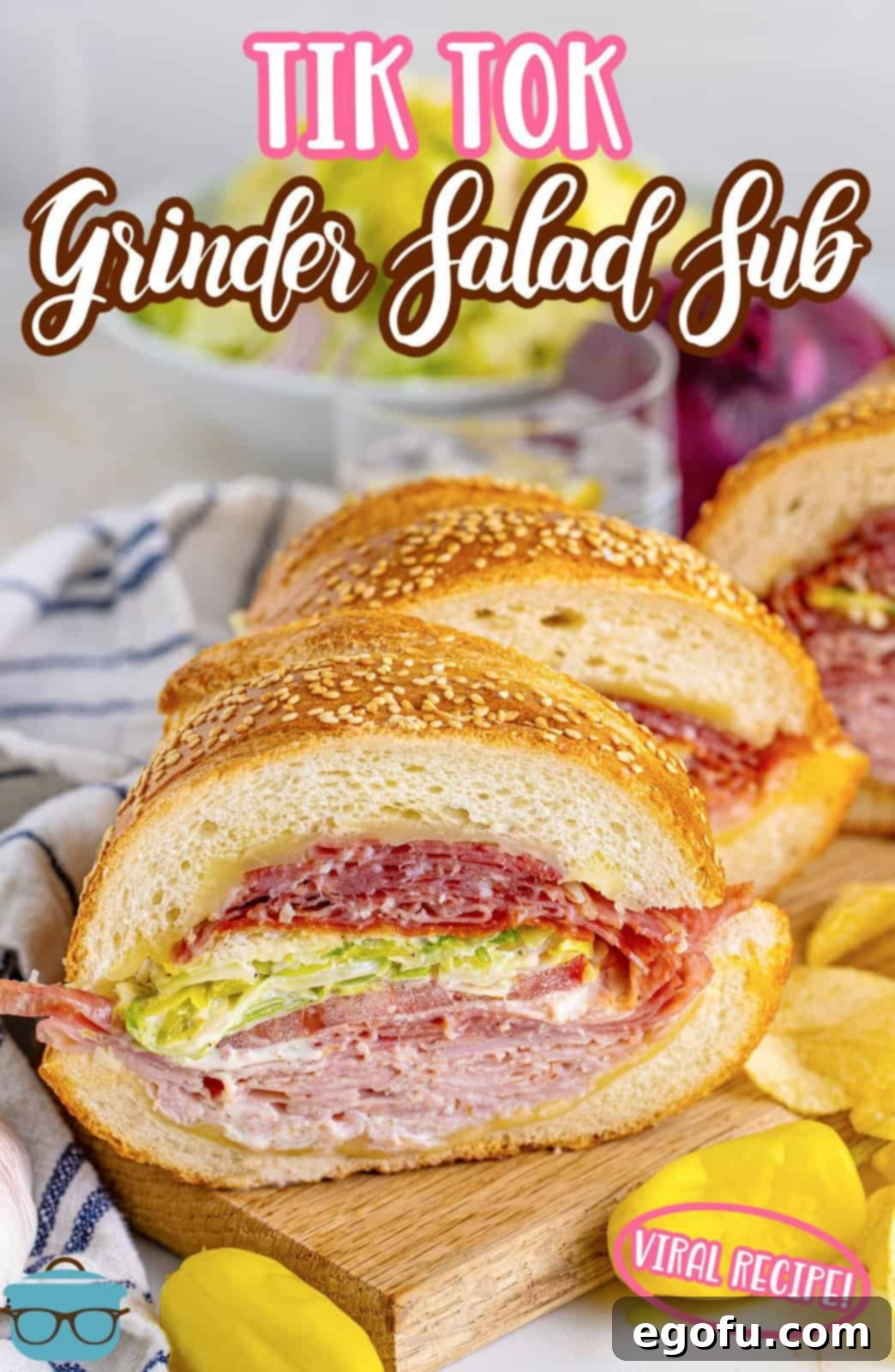 two slices of grinder salad sandwiches on a wooden cutting board with potato chips on the side.