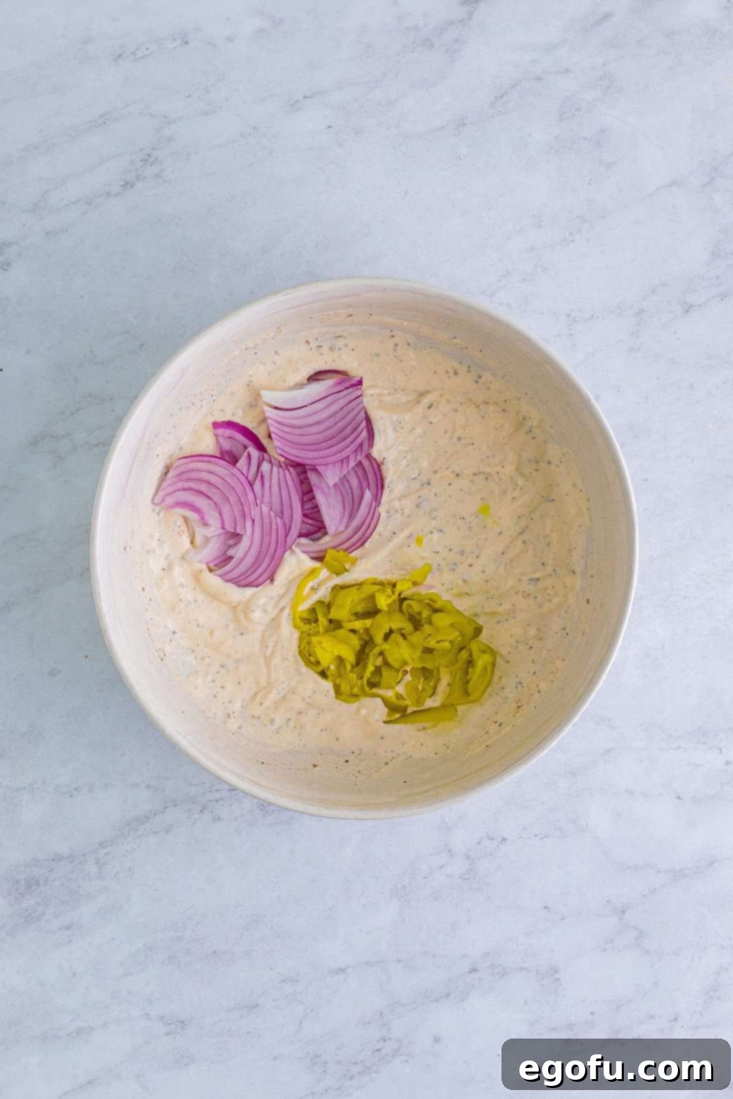 sliced red onion and sliced pepperoncini peppers added to mayonnaise mixture in bowl.