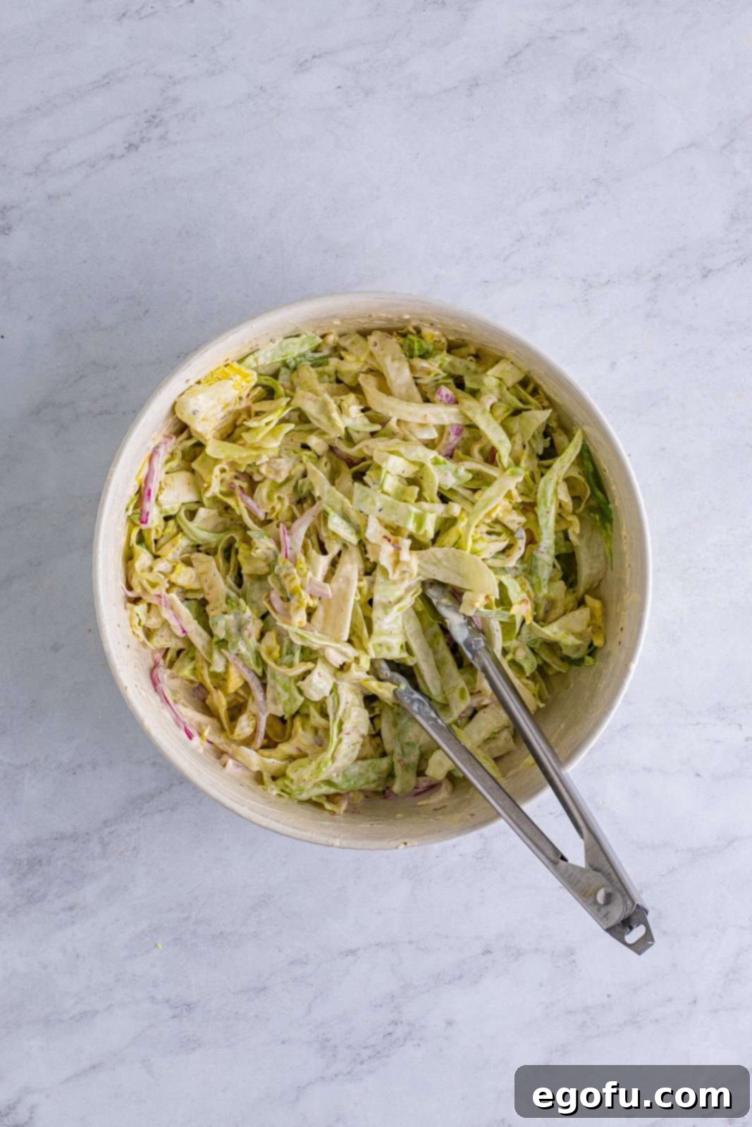 shredded lettuce added mayonnaise mixture in a bowl and being stirred together with tongs.