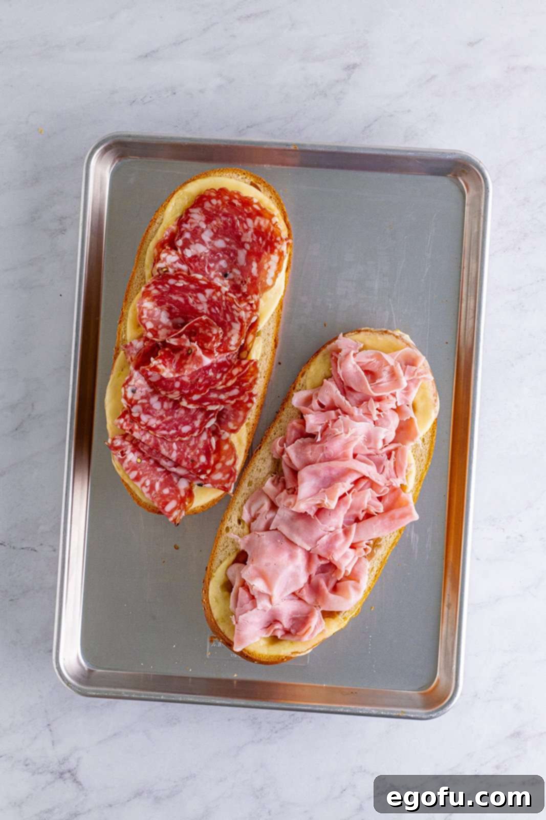 slices of ham on one side of the sub roll and sopressata salami slices on the other side of the sub roll.