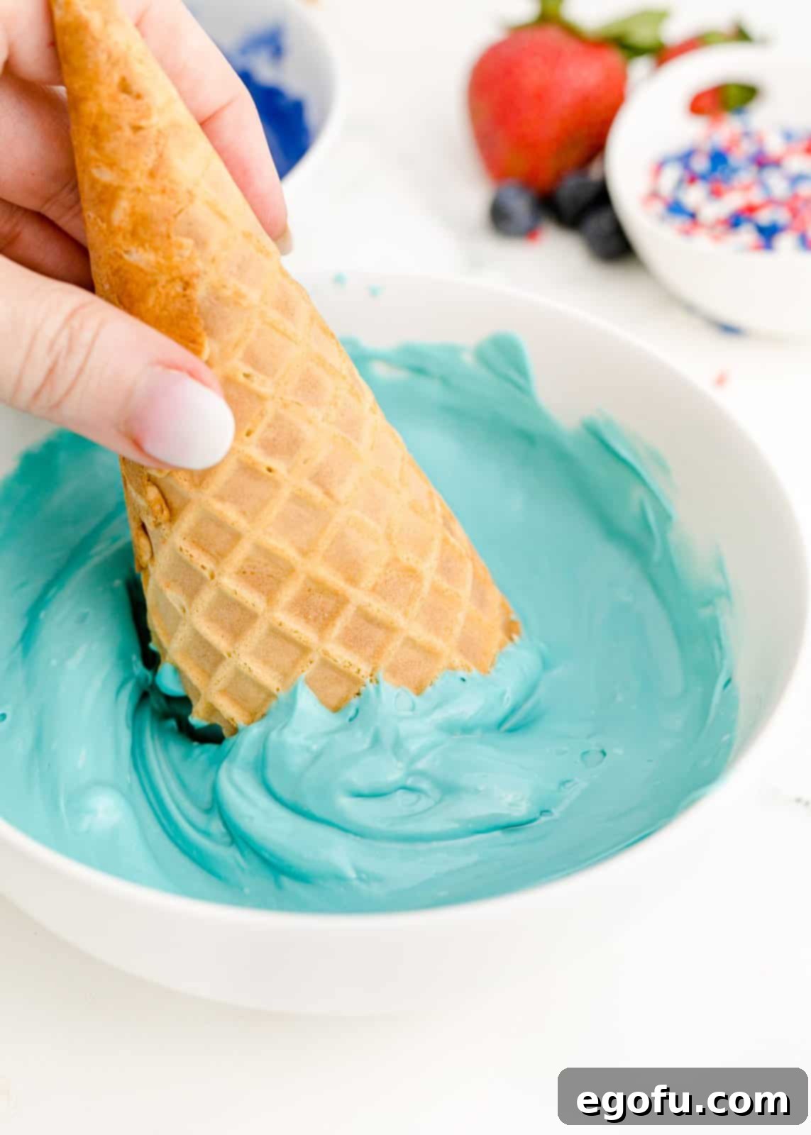 Waffle cone being dipped into candy melts.