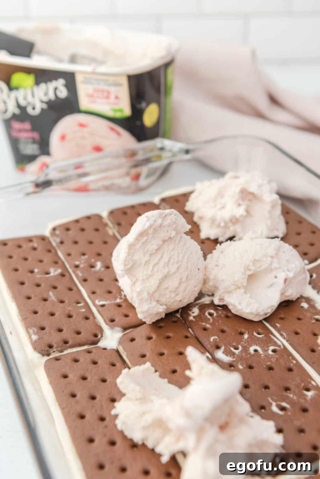 Ice cream dolloped over ice cream sandwiches in pan.