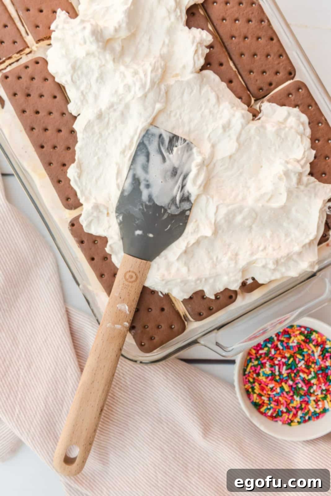 Whipped cream and cream cheese mixture being spread over ice cream sandwiches in pan.