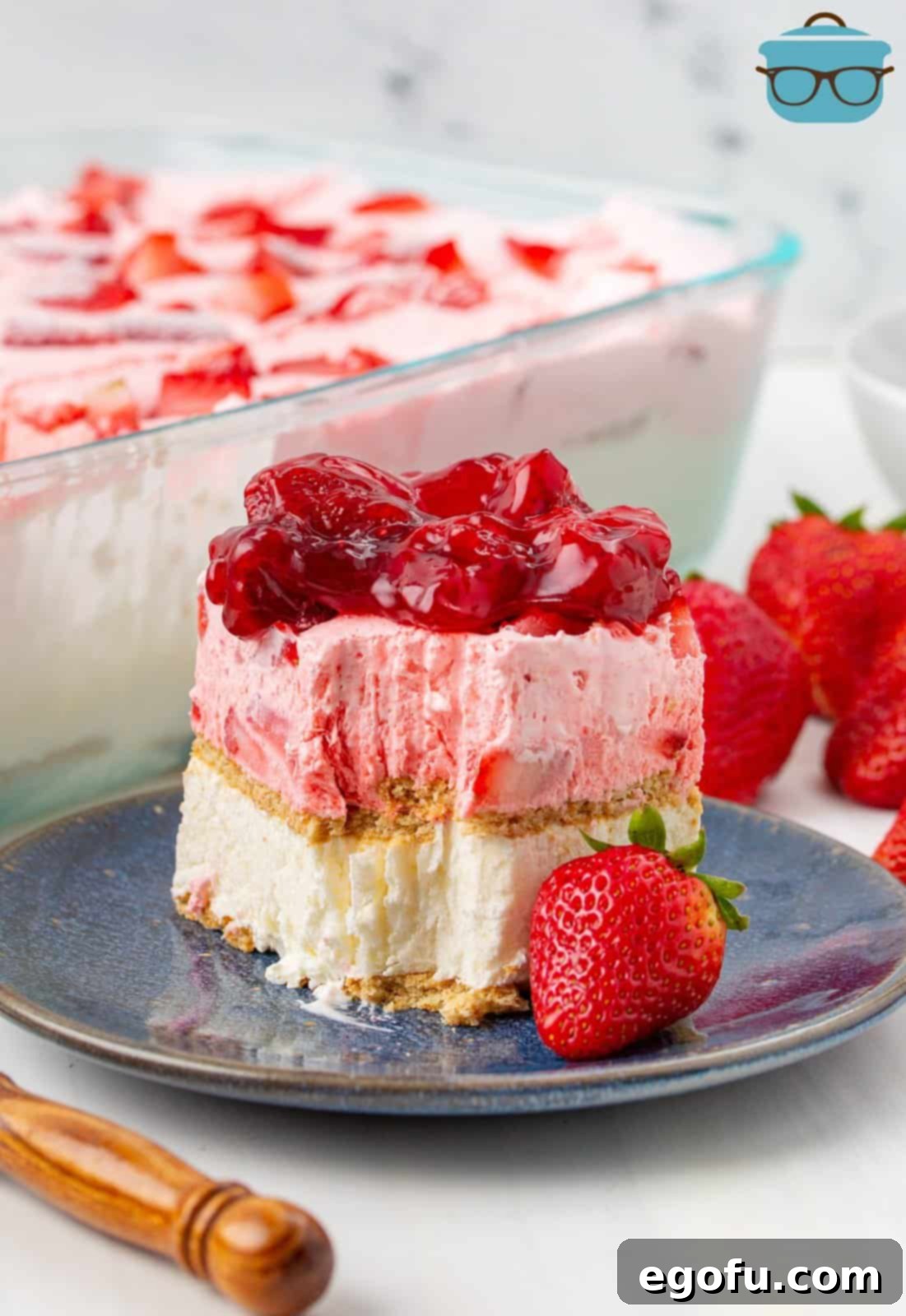 A perfectly sliced piece of Strawberry Icebox Cake on a dark plate, showing its distinct layers of creamy filling and graham crackers, with a bite taken out.
