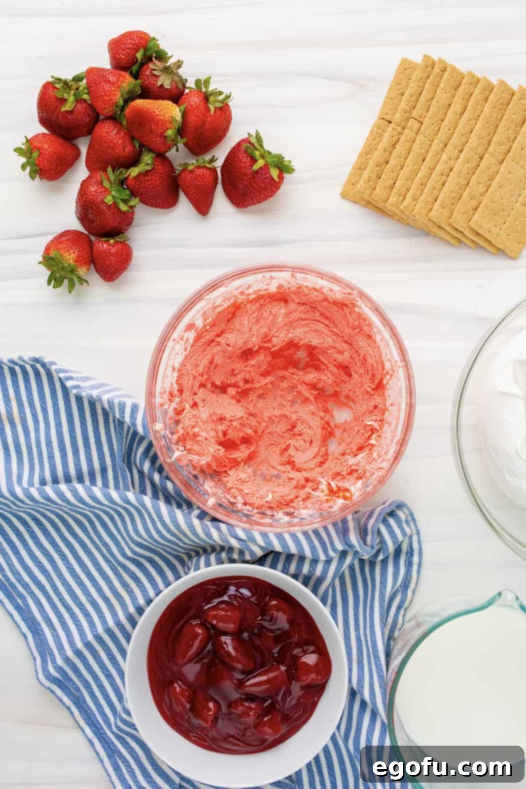 The second block of cream cheese blended smoothly with the dry strawberry Jell-O mix in a separate bowl, forming a vibrant pink base.