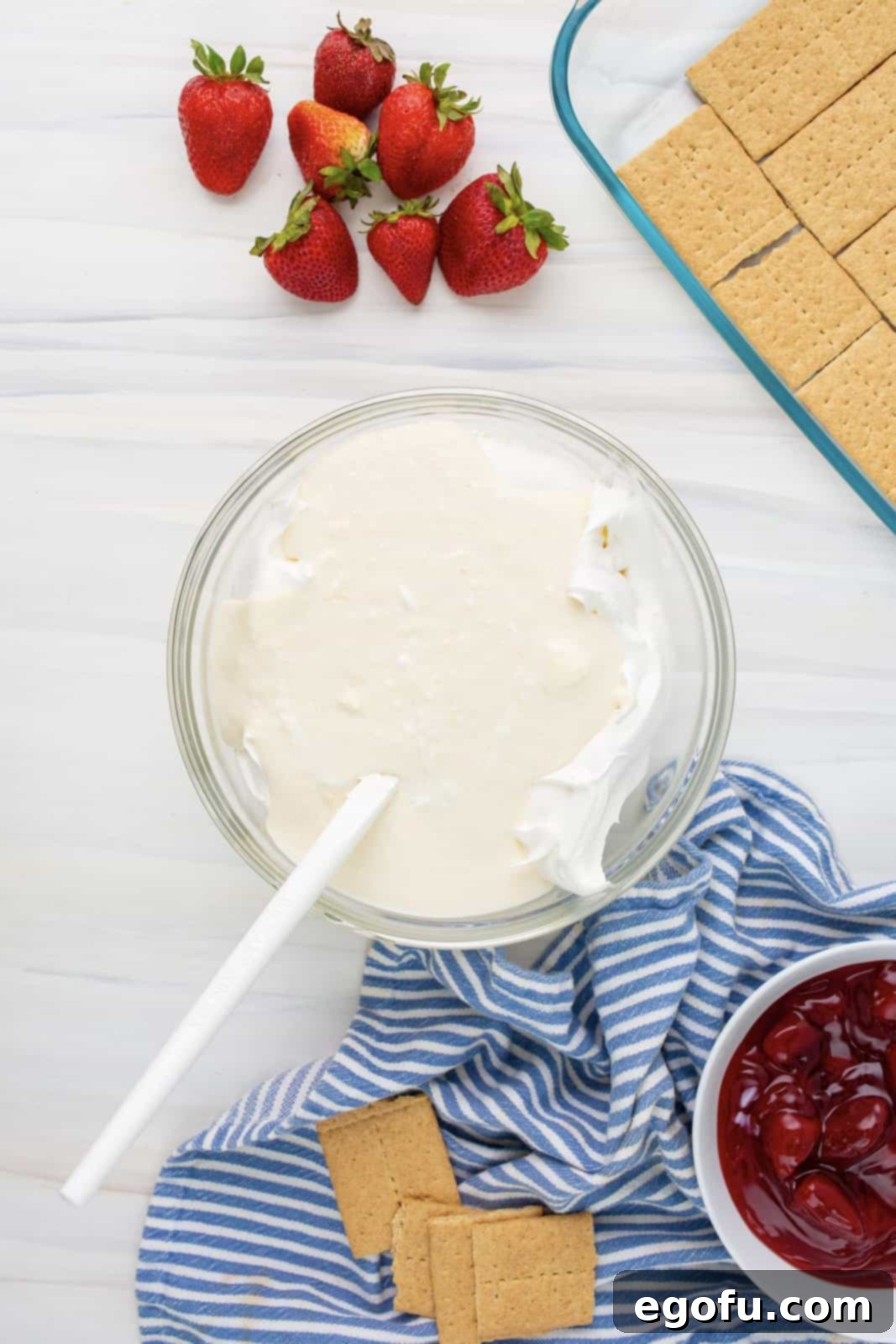 Half of the thawed Cool Whip being gently folded into the cheesecake pudding and cream cheese mixture, making it light and airy.