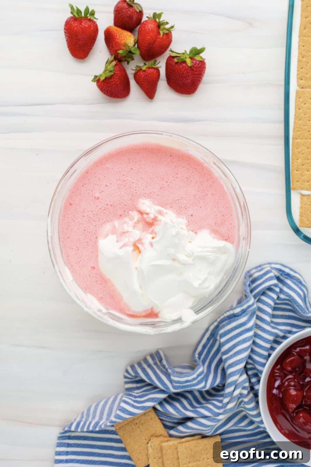 The second half of the Cool Whip being folded into the strawberry cream cheese and Jell-O mixture, enhancing its fluffy texture.
