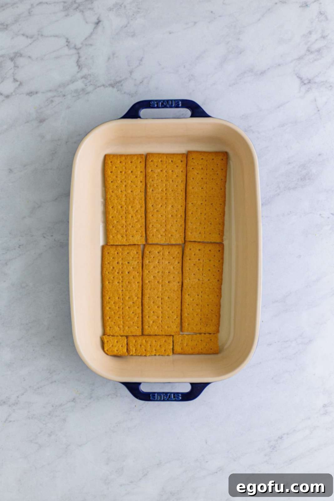 Graham crackers neatly arranged to form the first layer at the bottom of a 9x13-inch baking dish, some broken to fit.