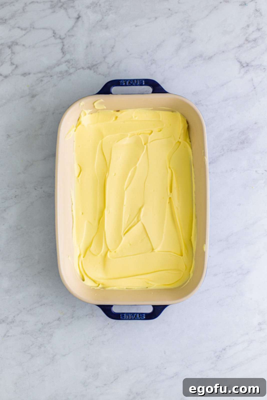 A smooth, creamy layer of banana pudding mixture spread evenly over the graham crackers in the baking dish, forming the second layer.