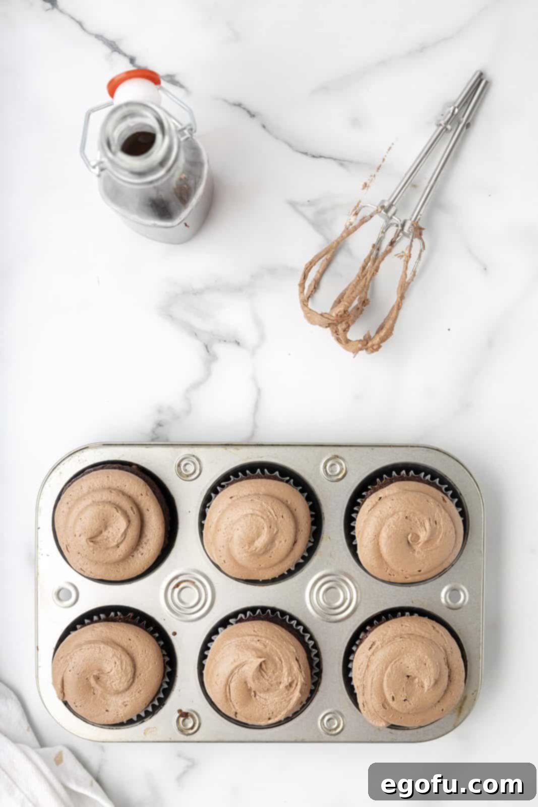 A smooth, generous swirl of chocolate marshmallow frosting is expertly piped onto a cooled cupcake.