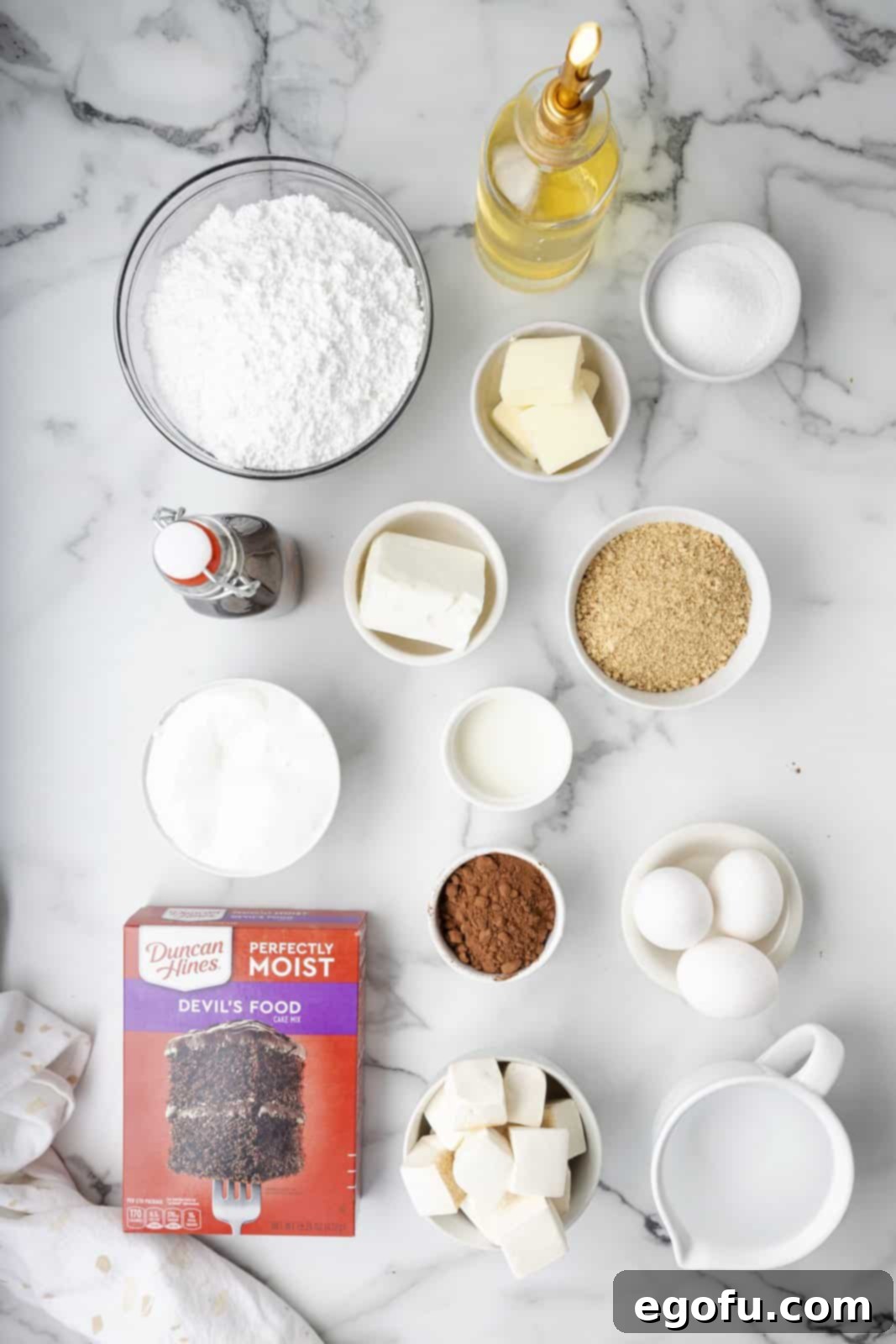 All the ingredients neatly laid out: graham cracker crumbs, granulated sugar, butter, chocolate cake mix and its required ingredients, salted butter, shortening, marshmallow fluff, powdered sugar, cocoa powder, milk, vanilla extract, and marshmallows.