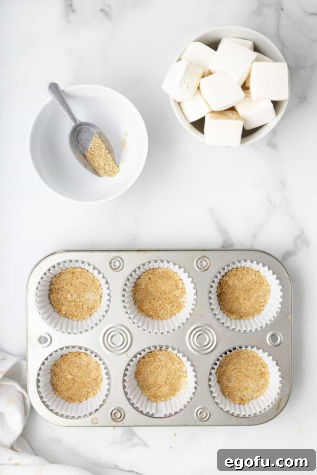 The graham cracker mixture is pressed down firmly into paper liners nestled in a cupcake tin, forming the crust.