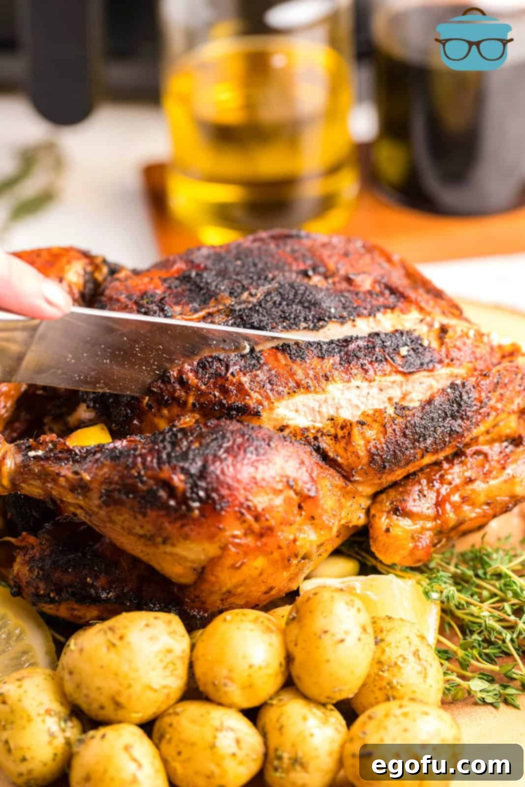 A knife slicing into the succulent Air Fryer Whole Roasted Chicken on a wooden board, garnished with fresh herbs and served alongside golden potatoes.