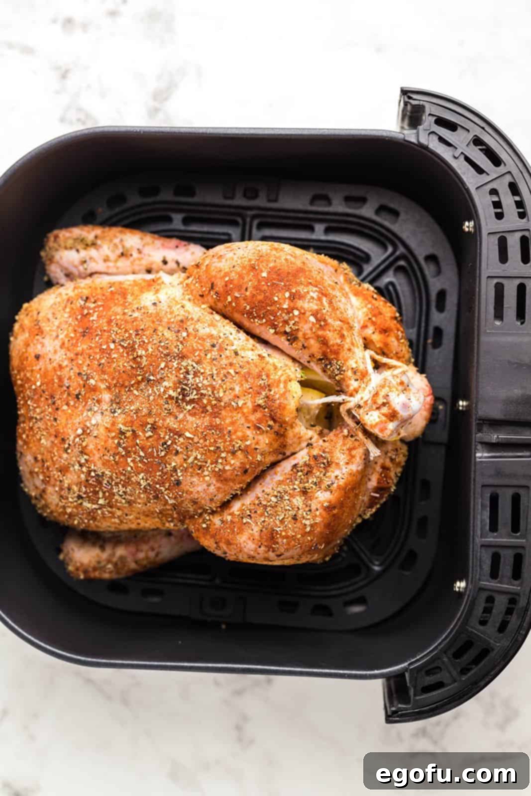 A whole seasoned chicken placed inside an air fryer basket, ready for cooking.