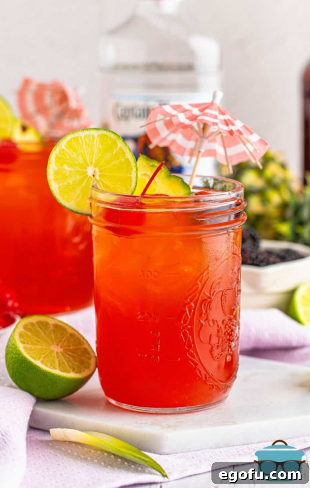 Rum Runner Cocktail in a mason jar, surrounded by fresh fruit garnishes and a mini umbrella, ready to be enjoyed on a hot day.